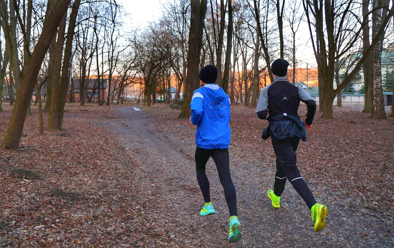 Two adults jogging in a park during fall, wearing athletic gear.